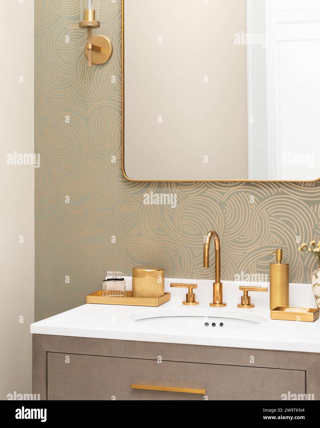 Un lavandino del bagno con rubinetto e decorazioni dorate, carta da parati a motivi geometrici, ripiano in marmo bianco e armadio in pelle di serpente. Foto Stock