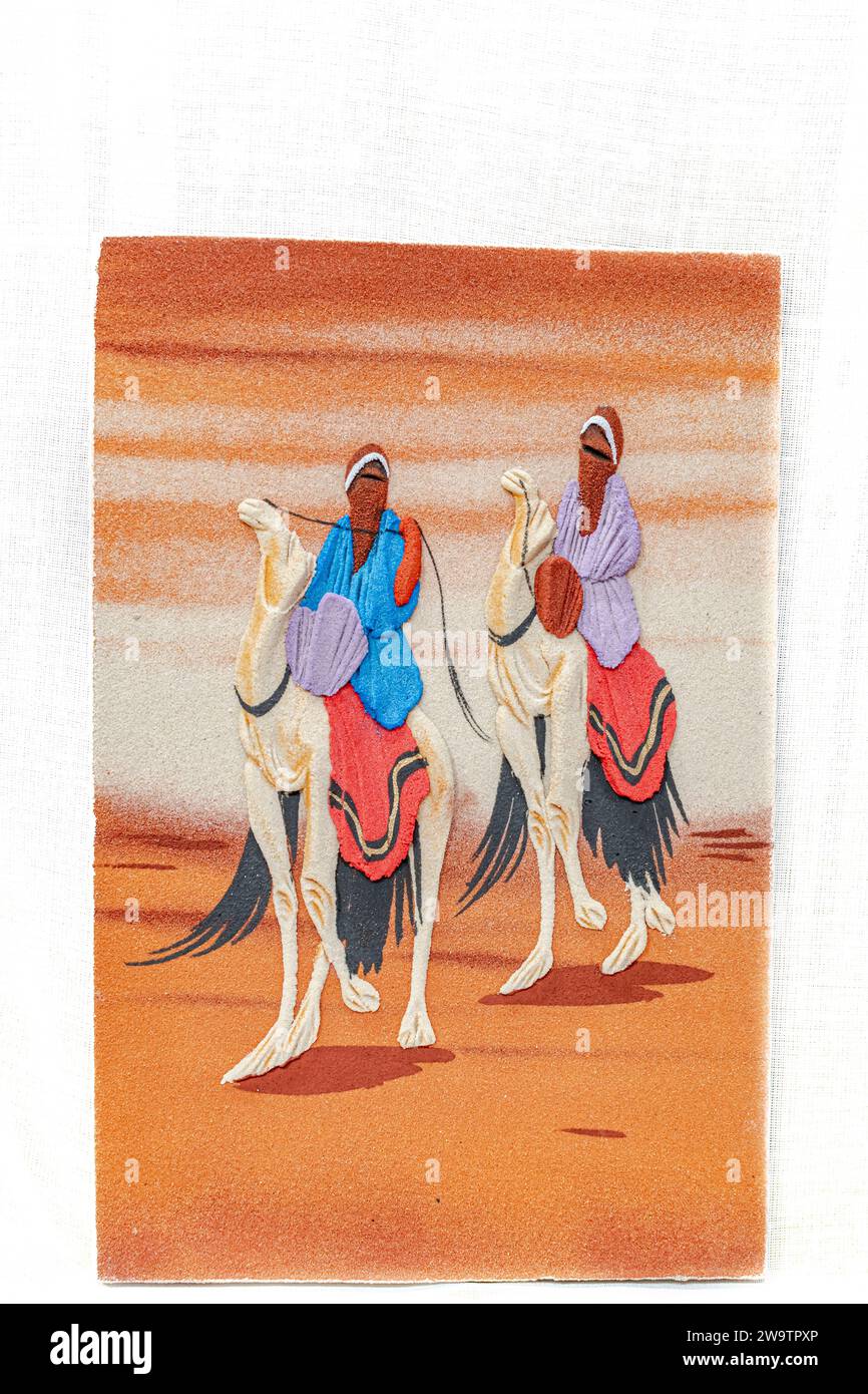 Un dipinto di sabbia in rilievo di due tuareg che indossano abiti tradizionali e sciarpe per la testa in cammelli dromedari bianchi che camminano nel Sahara Foto Stock