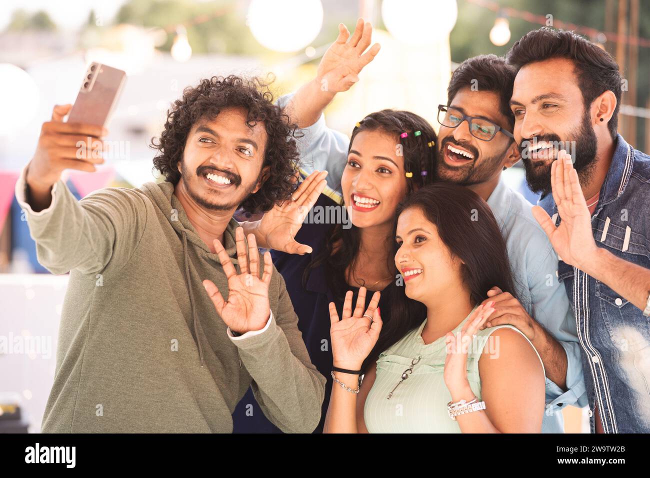 Gruppo di amici che parla in videochiamata o chat durante la festa serale in terrazza - concetto di comunicazione con smartphone, incontro virtuale e. Foto Stock