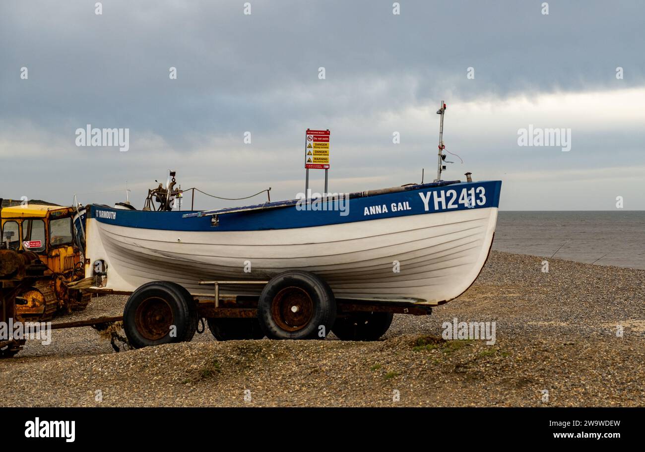 Weybourne, Norfolk, Regno Unito – dicembre 29 2023. Tradizionale barca da pesca in legno e trattore, su una spiaggia di ciottoli Foto Stock