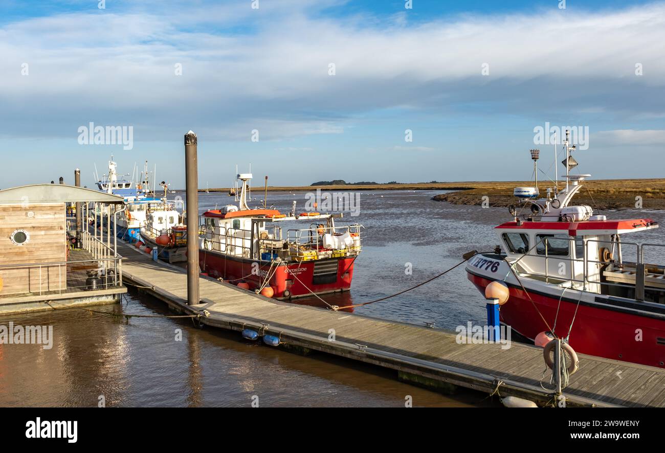 Wells-Next-the-SEA, Norfolk, Regno Unito - dicembre 29 2023. Barche da pesca legate a un pontile o a un molo di legno nel porto durante la bassa marea Foto Stock