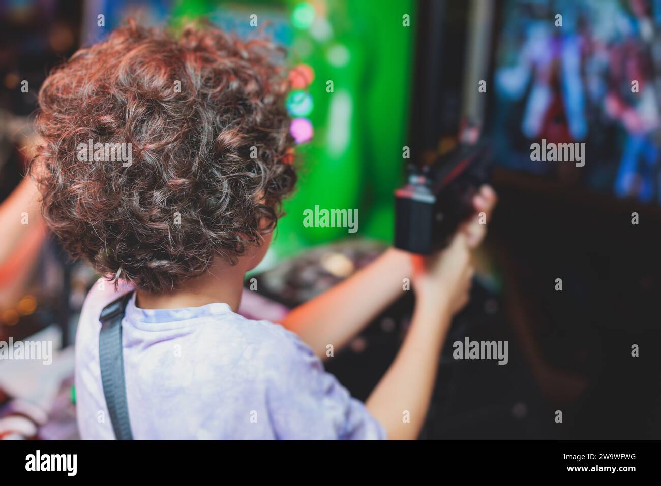 I bambini giocano alle slot machine nel parco divertimenti a tema, i bambini giocano con una macchina da gioco arcade, corse e sparatutto alla fiera, gli adolescenti si divertono a giocare Foto Stock