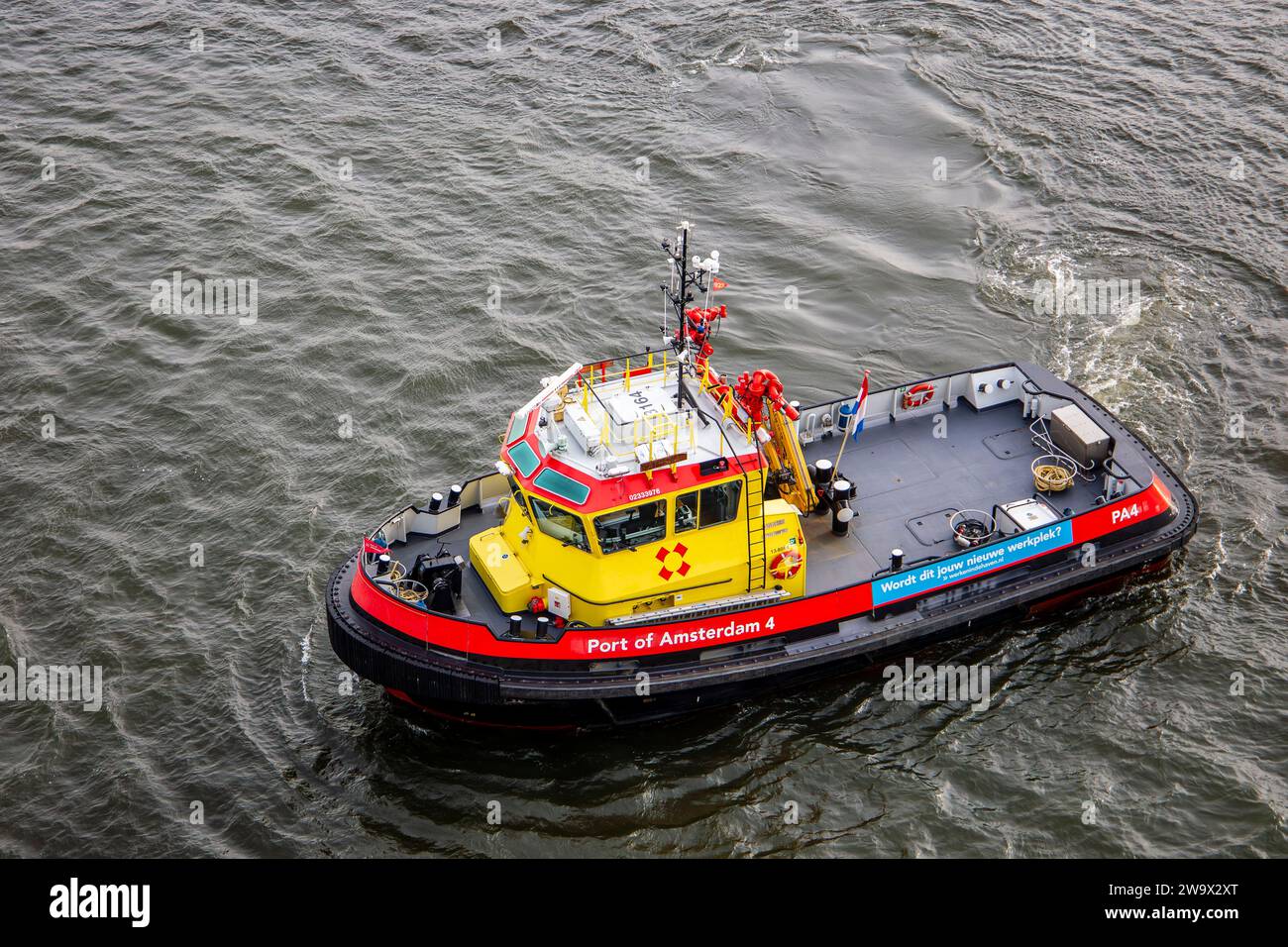 Un rimorchiatore dal porto di Amsterdam naviga attraverso il fiume, mostrando il suo robusto design giallo e rosso per l'assistenza marittima Foto Stock