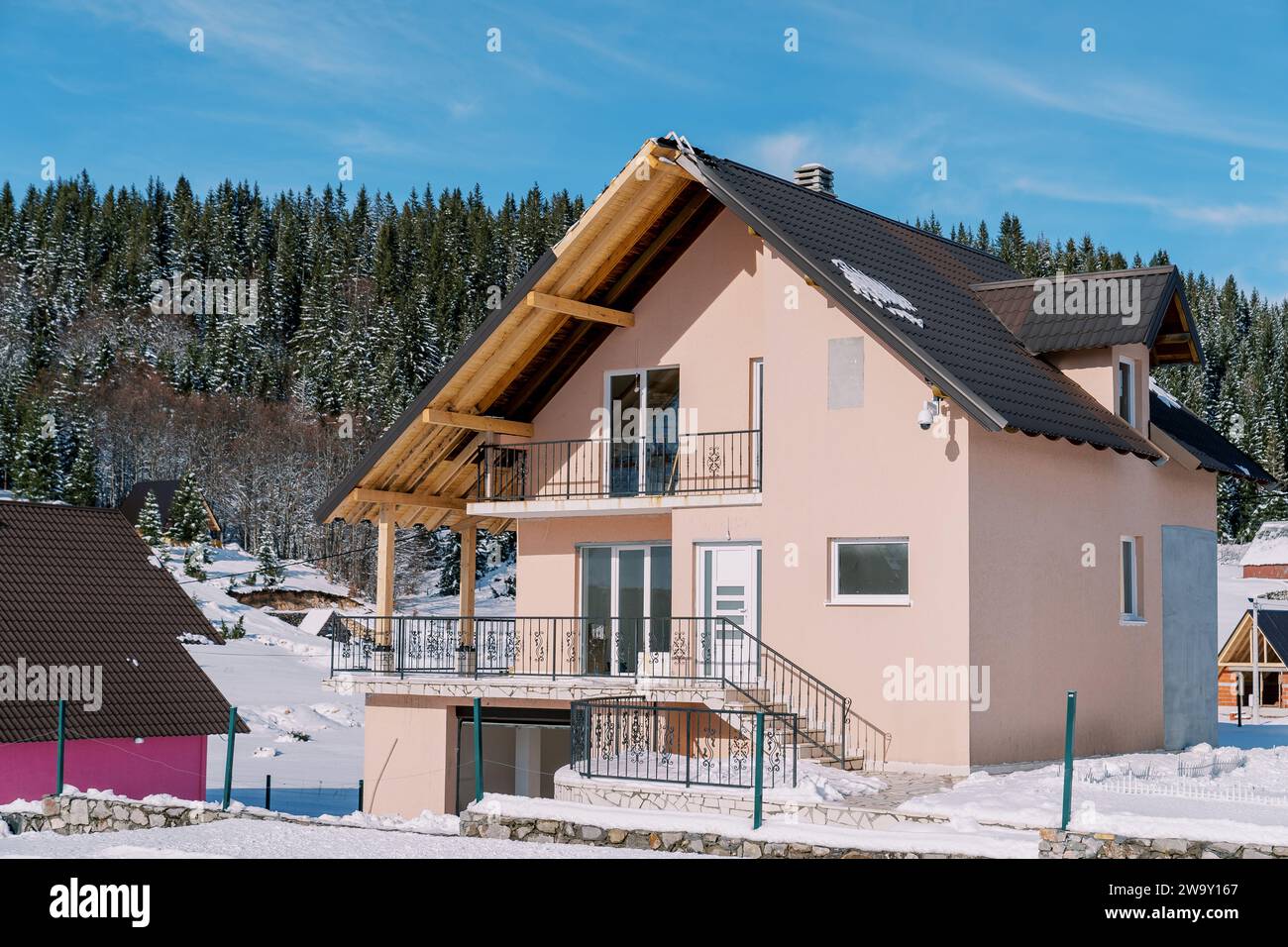 Casa rosa a due piani in un villaggio innevato ai margini di una foresta di conifere Foto Stock
