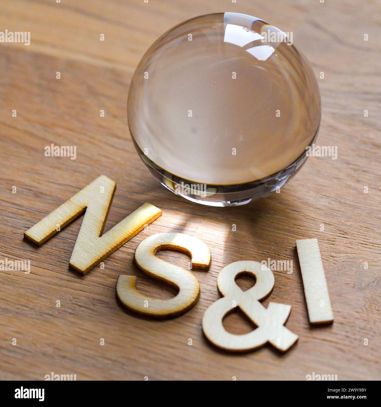 NS&i in lettere di legno intorno a una sfera di cristallo di vetro, su una superficie di legno con luce proveniente da una finestra che splende Foto Stock