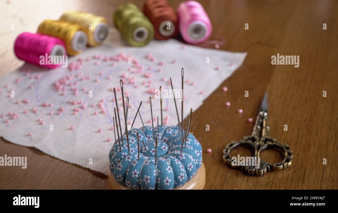Armonia artigianale: Progetto di ricamo con perline con fili di seta su tavolo in legno Foto Stock