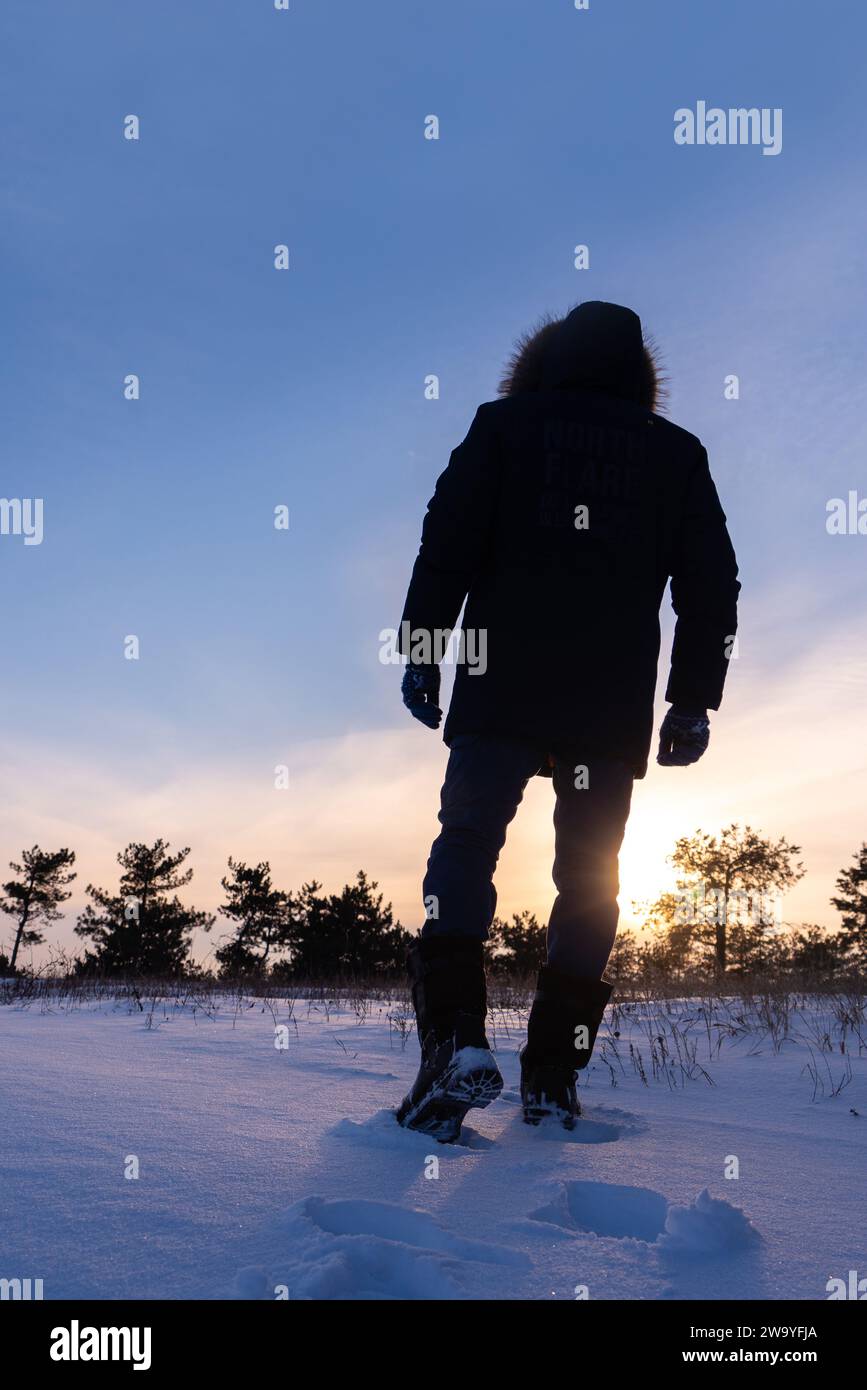 Un viaggiatore con gli scarponi cammina lungo una strada invernale innevata. Foto Stock