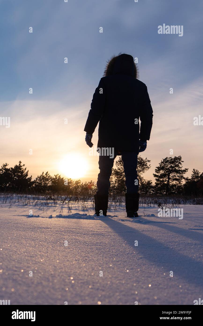 Un viaggiatore con gli scarponi cammina lungo una strada invernale innevata. Foto Stock