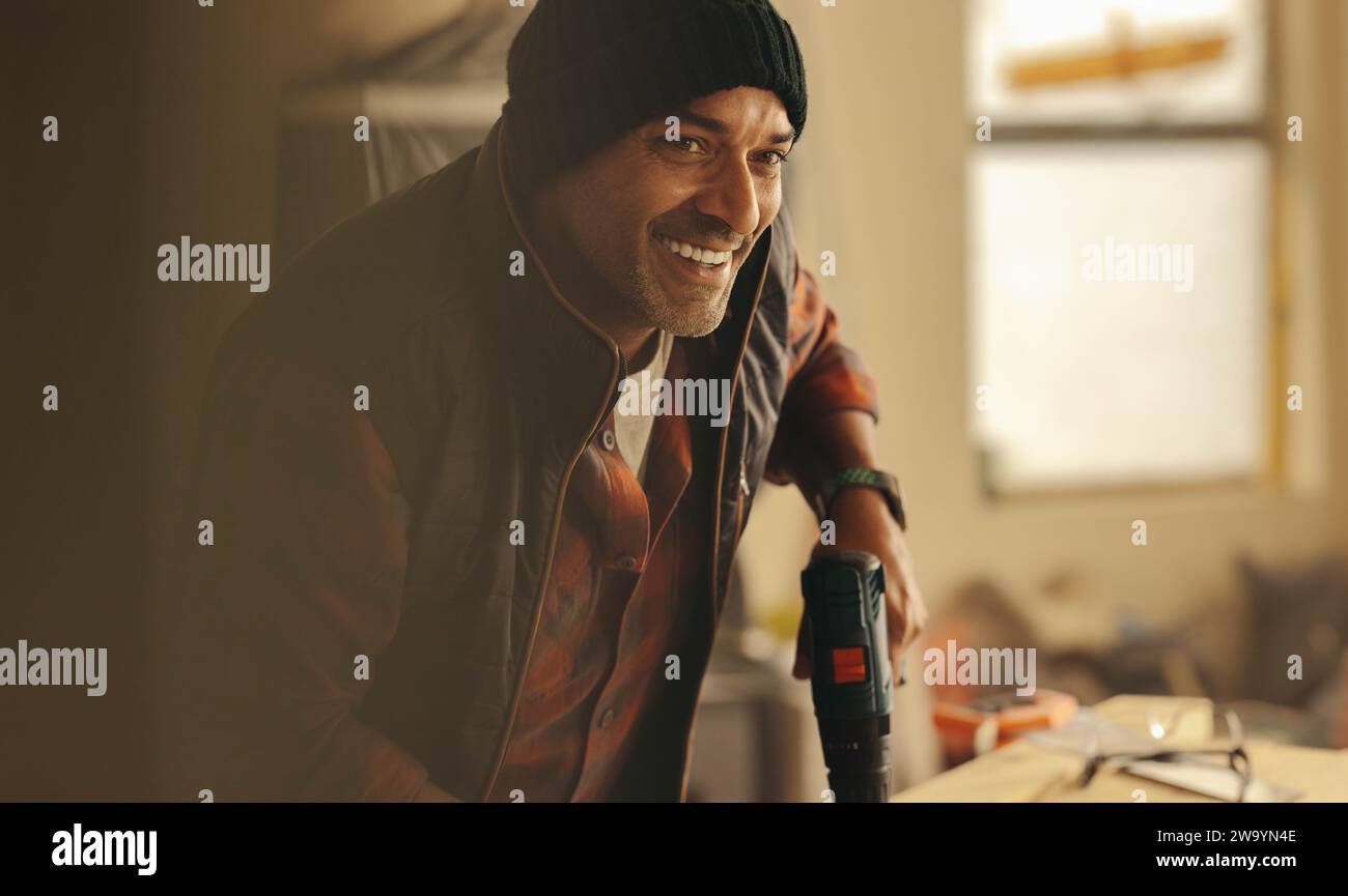 Happy falegname fai-da-te che ha rimodellato la sua cucina per un progetto di ristrutturazione della casa. Sta usando una pistola di perforazione e sta lavorando per aggiornare l'abitacolo. Uomo abile smi Foto Stock