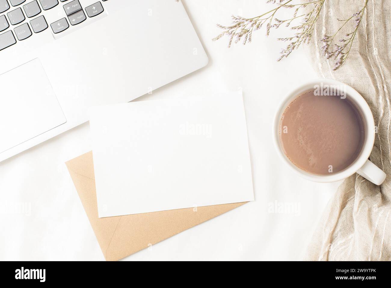 Tazza da caffè, computer portatile, busta con scheda vuota e fiori secchi su lino bianco. Ambiente di lavoro accogliente, comfort, concetto hygge. Vista dall'alto, piatto, mo Foto Stock