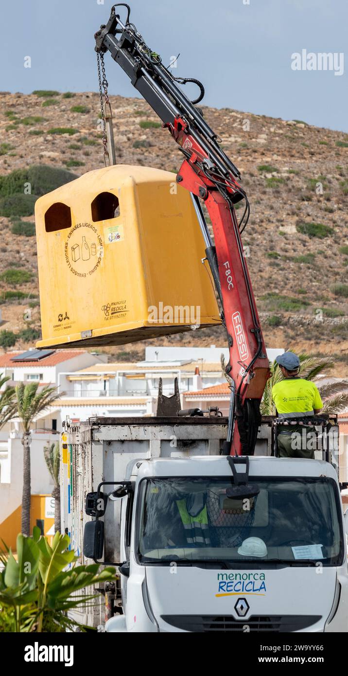 Menorca RECICLA camion che svuota un cestino di riciclaggio giallo nel villaggio di pescatori di Fornells Minorca Spagna. Foto Stock