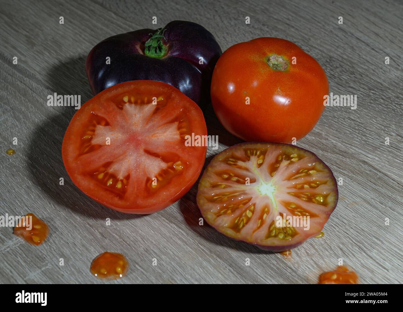 Un gruppo di quattro pomodori crudi appena raccolti, due pomodori interi e due tagliati a metà, con alcuni spruzzi di succo di pomodoro e i loro semi o semi Foto Stock