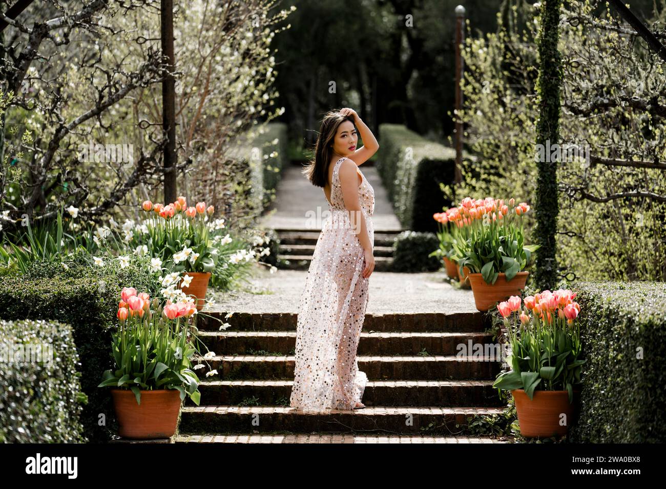 Bella Fit Curvy giovane donna asiatica Sheer paillettes abito in piedi in un giardino tulipani rosa Foto Stock