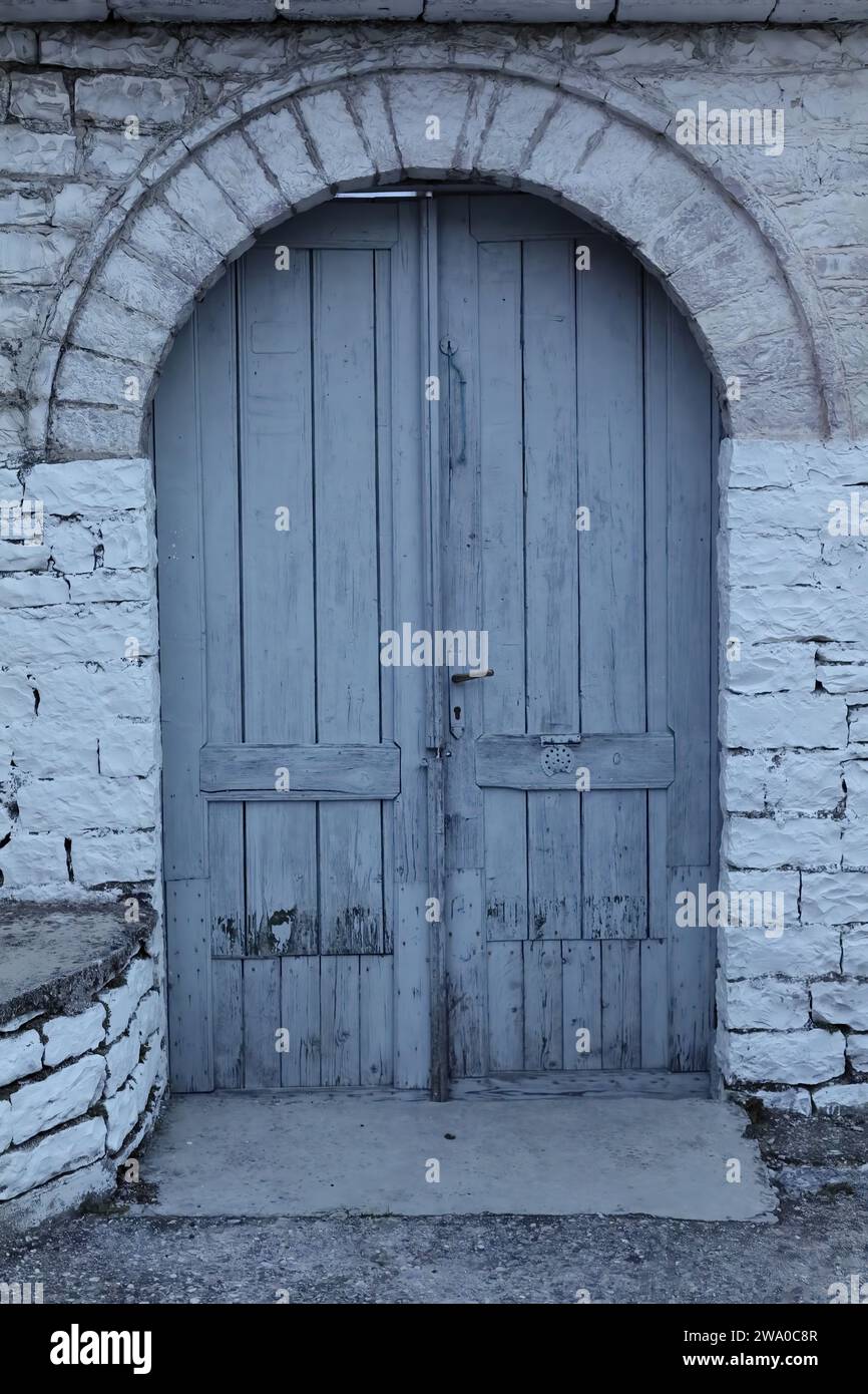187 Vecchio grigio-blu, doppia foglia, porta in legno ad arco rotondo tagliata in un muro di pietra, parte superiore della città vecchia. Gjirokaster-Albania. Foto Stock