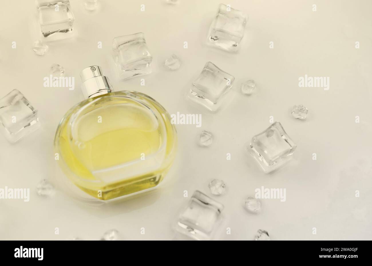 Bottiglia gialla di profumo femminile, fotografia oggettiva della bottiglia di profumo in cubetti di ghiaccio e acqua su tavolo bianco. Vista dall'alto. Foto del prodotto mockup, concetto di freschezza e aroma Foto Stock