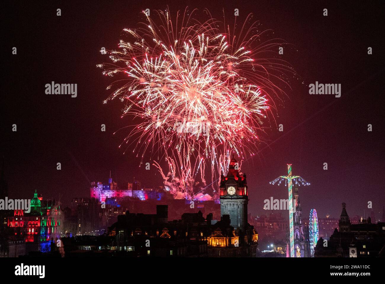 I fuochi d'artificio esplodono sopra il castello di Edimburgo e l'orologio Balmoral durante la festa di strada per il capodanno di Hogmanay a Edimburgo. Data immagine: Lunedì 1 gennaio 2024. Foto Stock