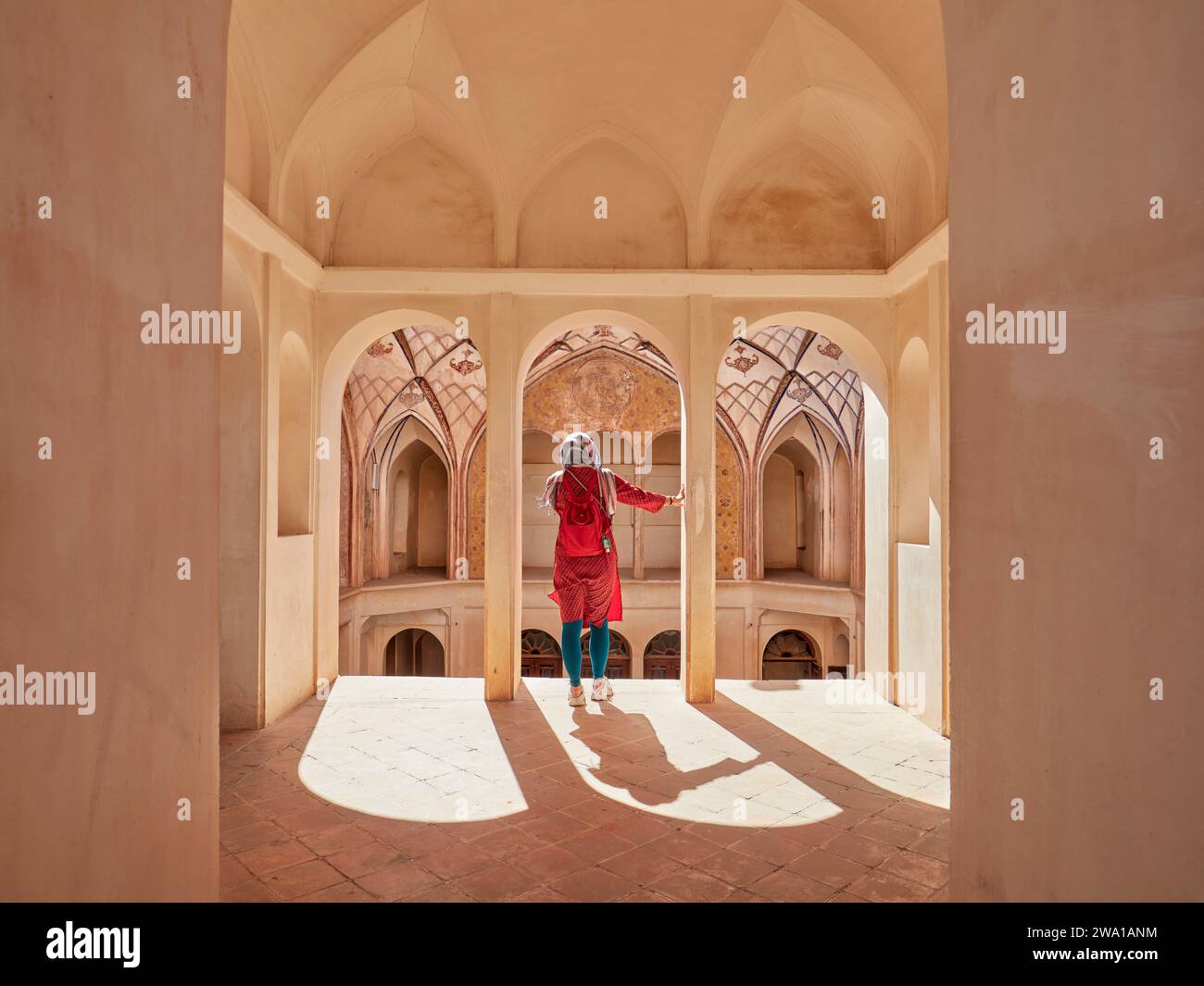 Donna in tunica rossa soggiorna ai margini di una terrazza al piano superiore nella Casa Tabatabaei, una dimora storica costruita intorno al 1880 a Kashan, Iran. Foto Stock