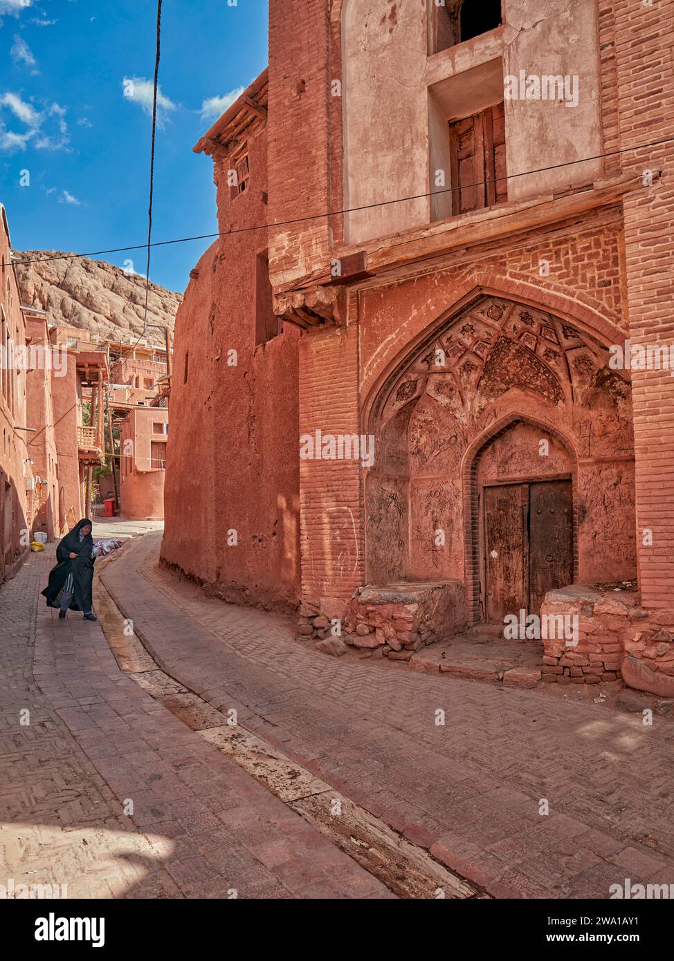 Una donna locale in abiti tradizionali cammina in una stradina stretta nello storico villaggio di Abyaneh, nella contea di Natanz, Iran. Foto Stock
