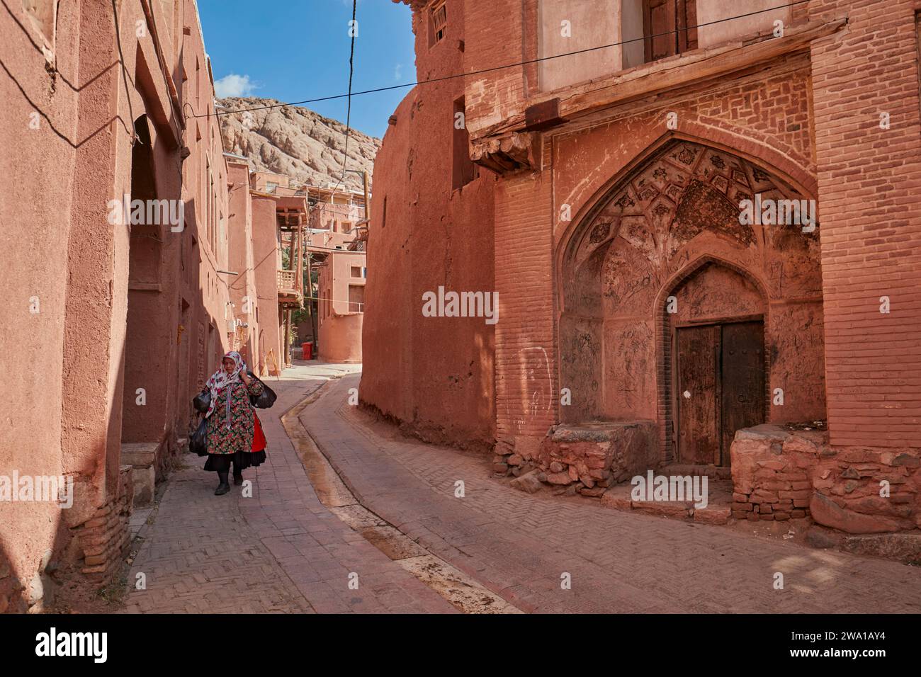 Una donna locale in abiti tradizionali cammina in una stradina stretta nello storico villaggio di Abyaneh, nella contea di Natanz, Iran. Foto Stock