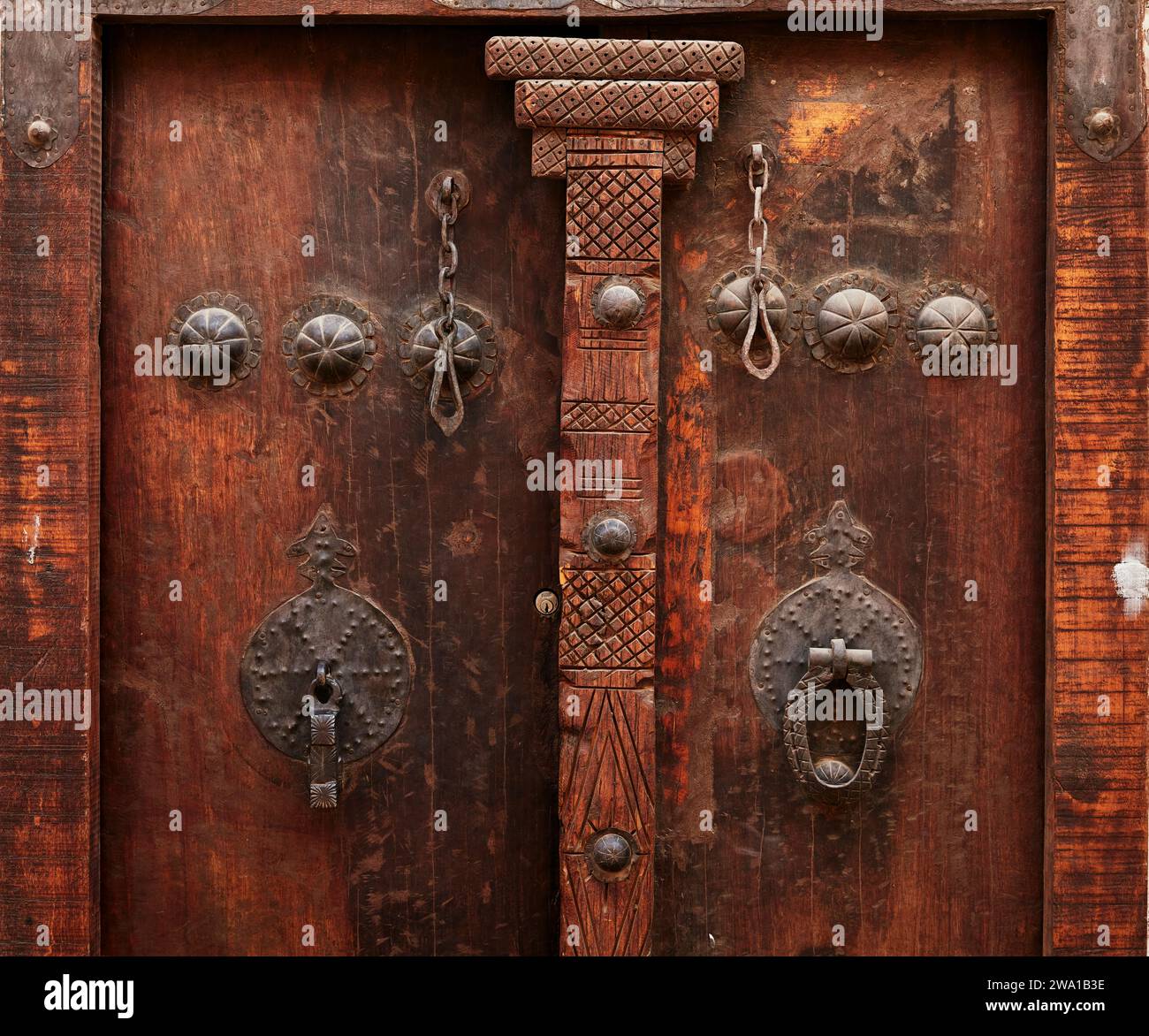 Dettaglio di una vecchia porta d'ingresso in legno di una casa con due diversi battitori - barra di metallo per gli uomini e anello di metallo per le donne. Kashan, Iran. Foto Stock