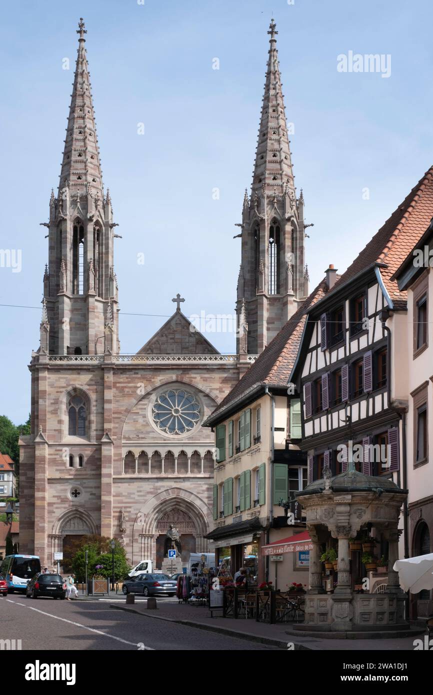 Chiesa con due torri dei Santi Pietro e Paolo e sulla destra il pozzo d'acqua a sei secchi in stile rinascimentale nel centro della città di Obernai, Francia Foto Stock