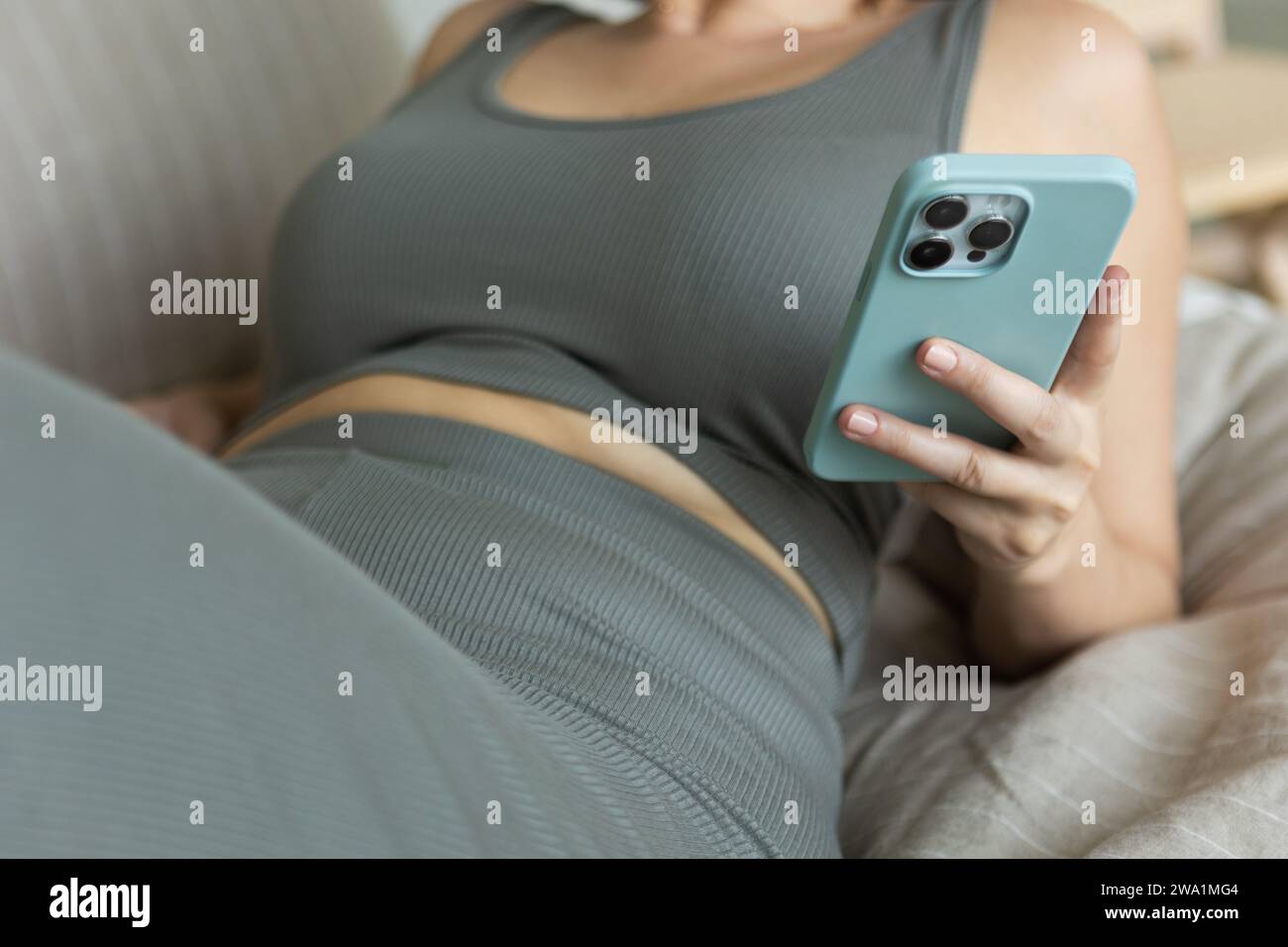 La donna scorre sullo smartphone mentre si rilassa in un set coordinato estetico Foto Stock