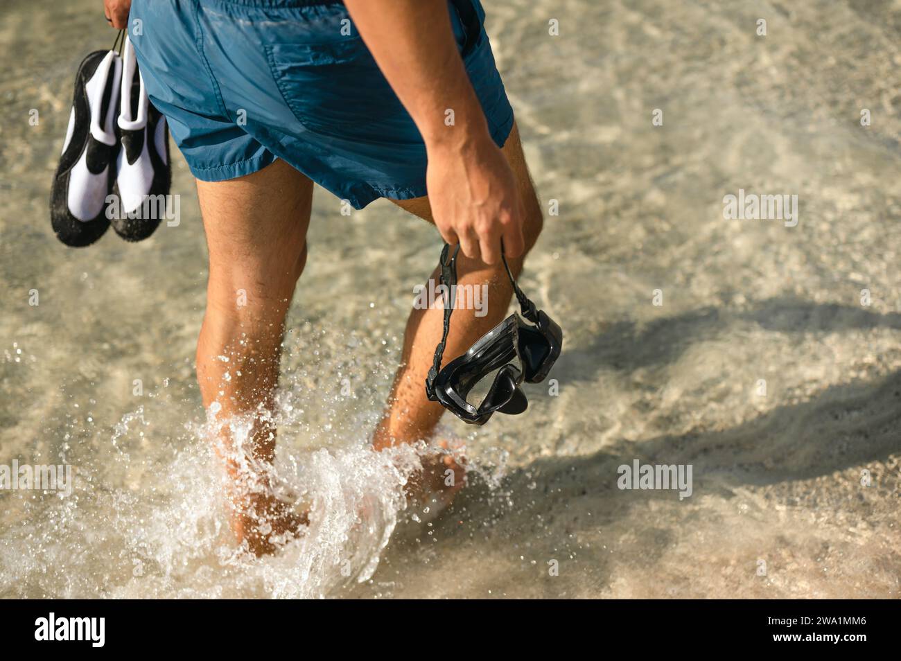 Uomo che cammina in acqua con maschera da snorkeling e scarpe da acqua lungo la spiaggia Foto Stock