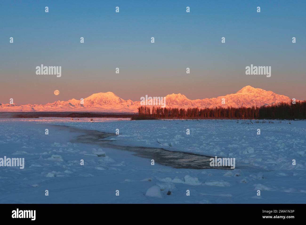La luna piena si erge dietro la catena dell'Alaska con Denali Foto Stock