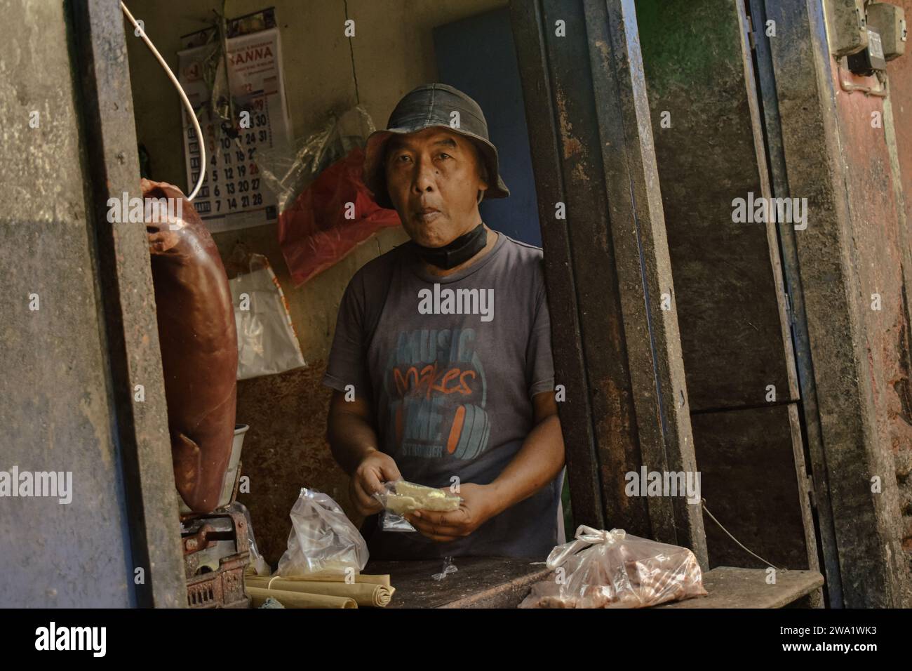 Malang, Indonesia, 01 gennaio 2024: Un venditore di carne al mercato sta facendo uno spuntino con i cracker guardando al futuro Foto Stock