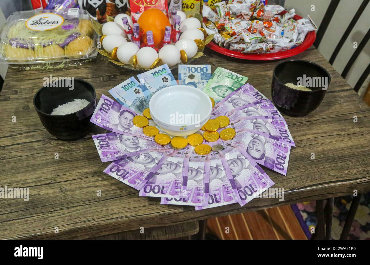 San Antonio, Filippine. 1 gennaio 2024: Le celebrazioni del Capodanno filippino sono piene di superstizioni, un patrimonio ricco di influenze cinesi, spagnole, cattoliche e pagane. Molti filippini si rivolgono a portafortuna e rituali per portare loro fortuna. Tra indossare caramelle rosse, salti di mezzanotte o rumori per allontanare gli spiriti maligni, molti creano una ciotola ricca di riso, monete, bollette, uova, buste rosse in numeri dispari, qualche volta acqua, frutta o alloro benedetto vicino a cioccolatini o frutta. Una versione locale del Feng shui credeva di liberare ricchezza e abbondanza. Crediti: Kevin Izorce/Alamy Live News Foto Stock