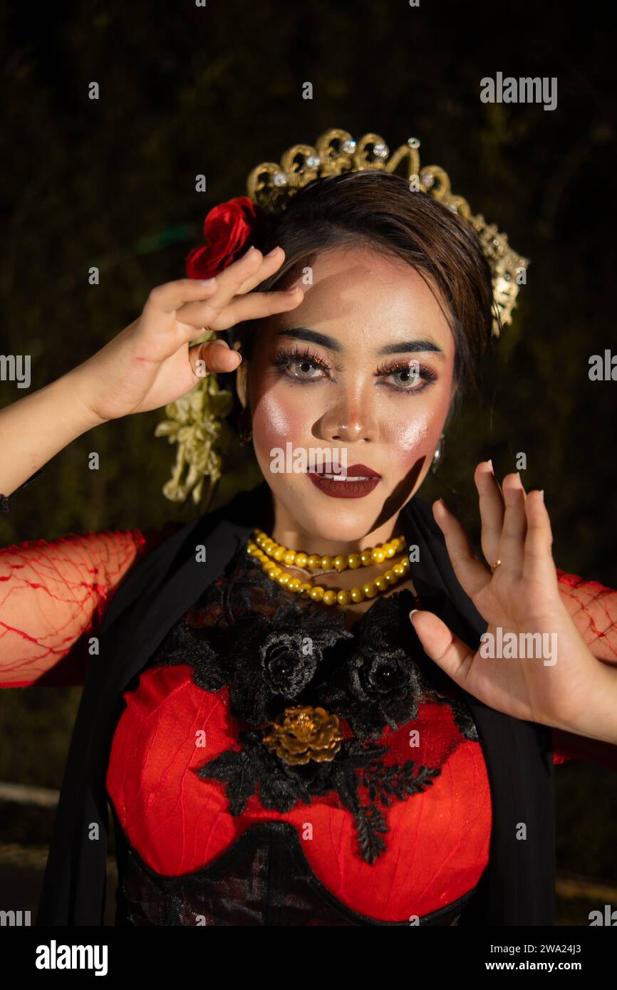 Una ballerina indonesiana in abiti rossi e una sciarpa nera posa con le dita molto ricci e belle di notte Foto Stock