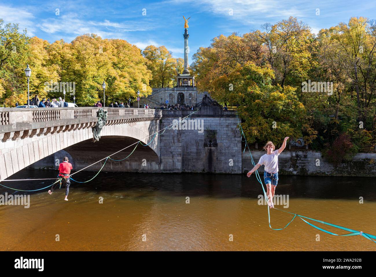 Un uomo si bilancia su una linea di slackline sull'Isar al ponte Luitpold nel sole autunnale, Monaco, Baviera, Germania Foto Stock