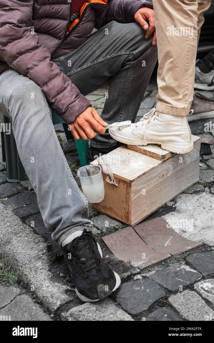 Cobbler pulizia e lucidatura delle scarpe bianche del cliente con spazzola. Scena stradale di Istanbul. Pulitore di scarpe che lavora sulla strada Turchia. Shiner. Foto Stock