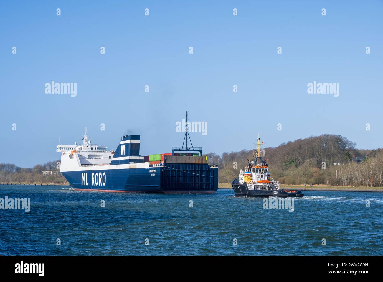 Ein Frachtschiff im Kiel Canal mit Schlepperunterstützung an einem windigen Wintertag Foto Stock