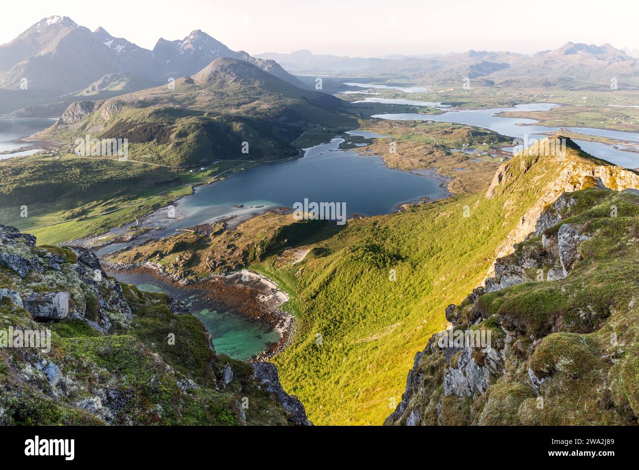 La luce del sole dorata bagna le valli verdeggianti e le insenature turchesi delle Isole Lofoten, Norvegia, con uno sfondo di maestose montagne Foto Stock