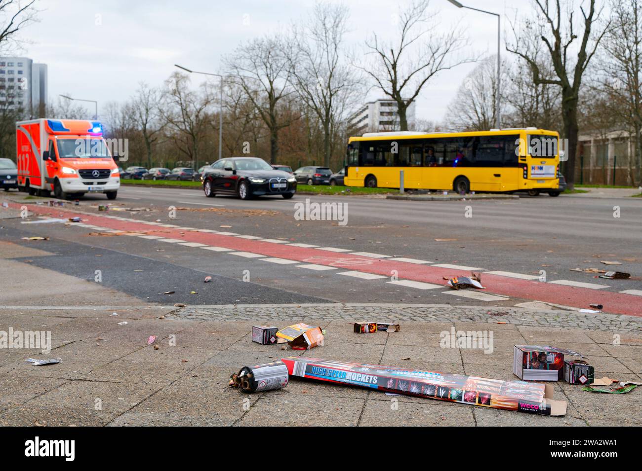 Berlino, Germania - 1° gennaio 2024: Scena stradale con fuochi d'artificio in primo piano e un'ambulanza dei vigili del fuoco sullo sfondo. Foto Stock
