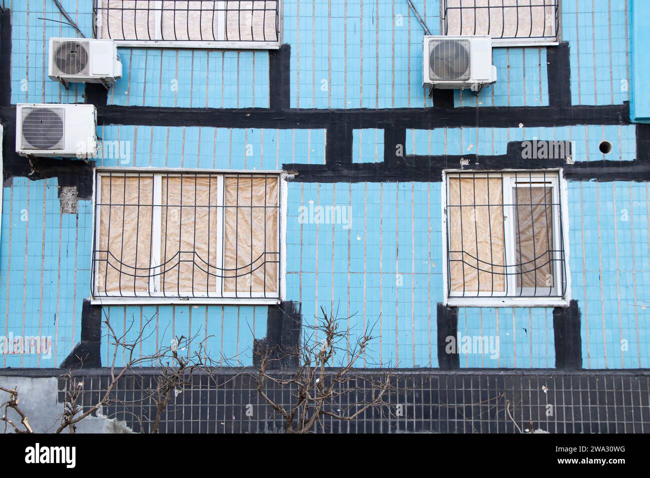 Edificio residenziale dopo un'ondata di esplosione con finestre rotte coperte di compensato, attacco di razzi in Ucraina, guerra Foto Stock