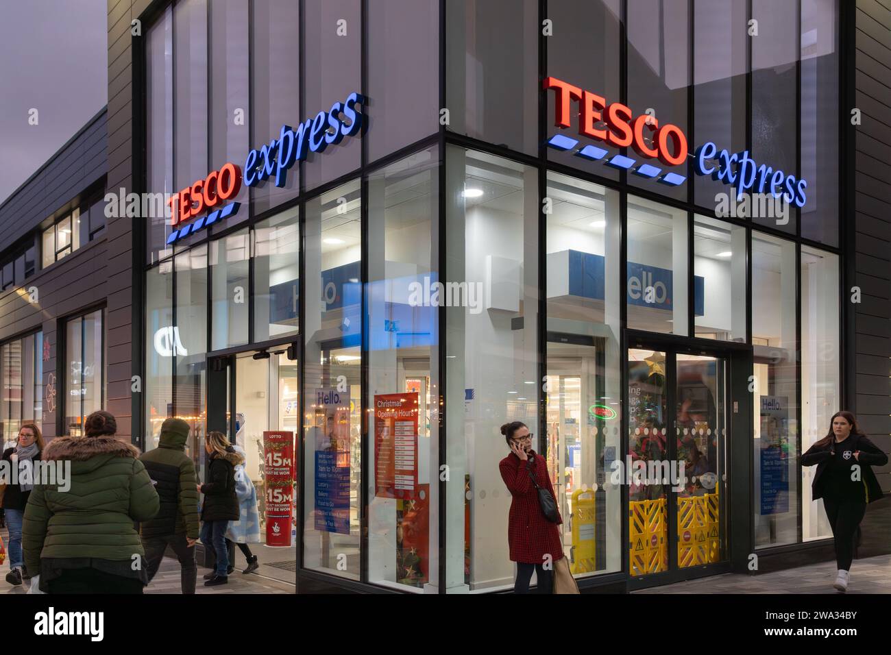 Gli acquirenti entrano e escono da un Tesco Express al crepuscolo nei centri commerciali di Basingstoke, Regno Unito. Tema: Costo della vita, inflazione alimentare, costo dello shopping Foto Stock