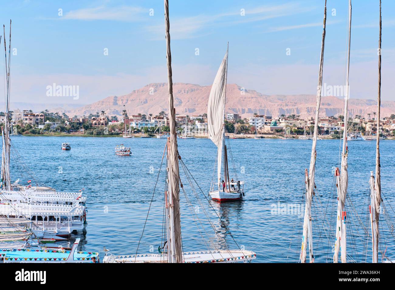 Luxor, Egitto - dicembre 26 2023: Tradizionali traghetti a motore e barche a vela in feluca ormeggiate lungo il Nilo Foto Stock