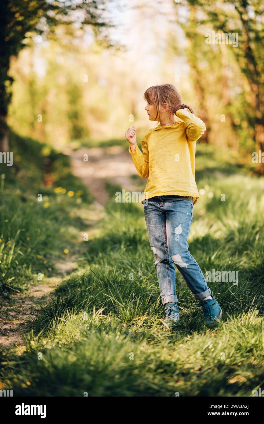 Ritratto all'aperto di una graziosa bambina nella foresta primaverile, che indossa camicetta verde e jeans Foto Stock