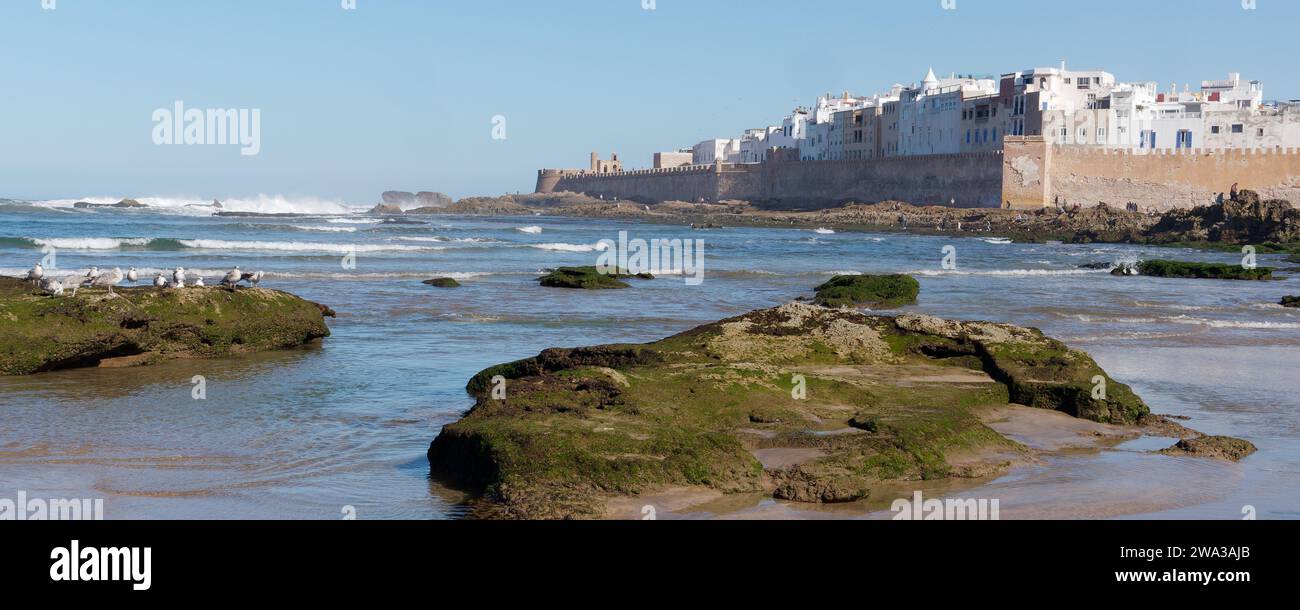 Spiaggia rocciosa con le mura della città e la storica medina alle spalle nella città di Essaouira, Marocco, 1 gennaio 2024 Foto Stock