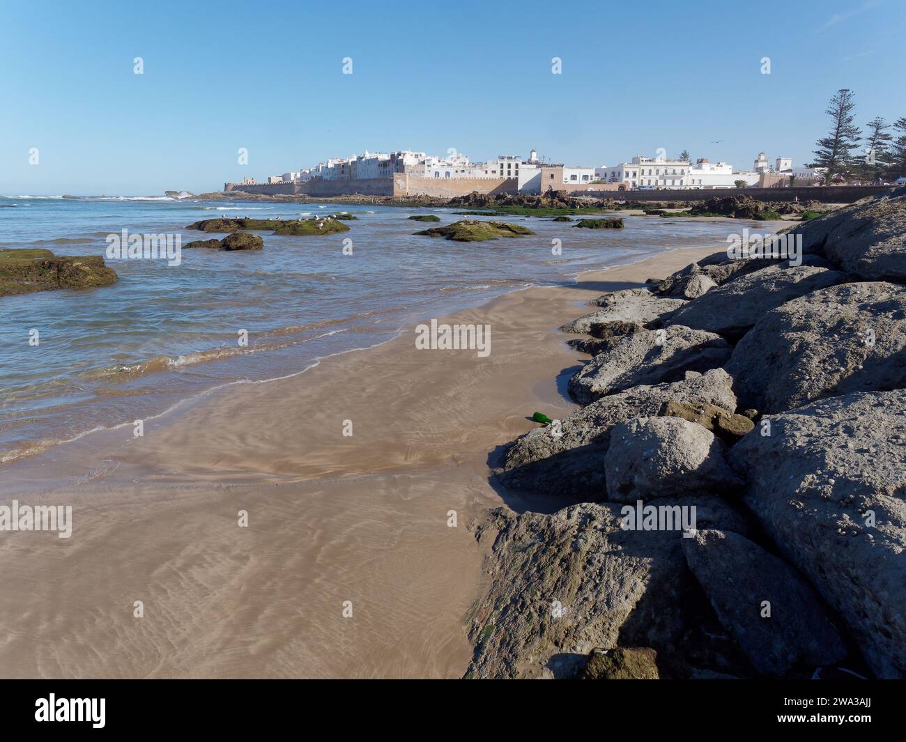 Spiaggia rocciosa con le mura della città e la storica medina alle spalle nella città di Essaouira, Marocco, 1 gennaio 2024 Foto Stock