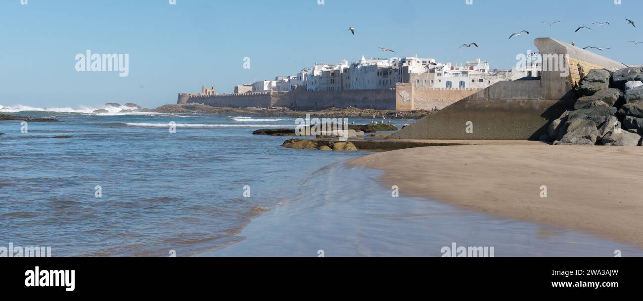 Spiaggia rocciosa con le mura della città e la storica medina alle spalle nella città di Essaouira, Marocco, 1 gennaio 2024 Foto Stock