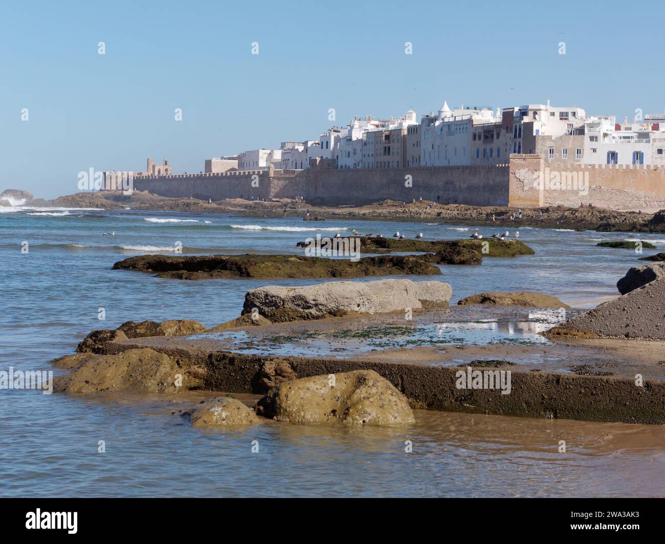 Spiaggia rocciosa con le mura della città e la storica medina alle spalle nella città di Essaouira, Marocco, 1 gennaio 2024 Foto Stock