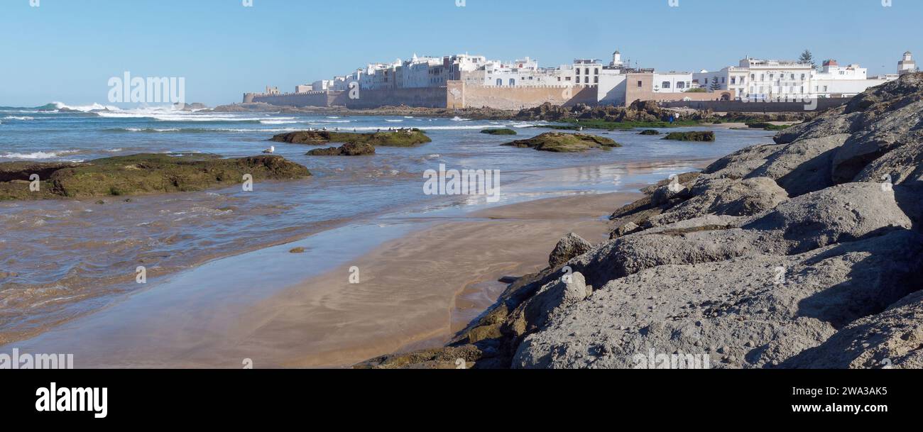 Spiaggia rocciosa con le mura della città e la storica medina alle spalle nella città di Essaouira, Marocco, 1 gennaio 2024 Foto Stock