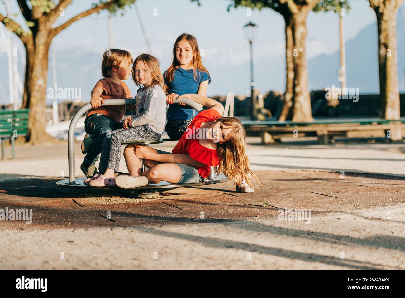 Gruppo di quattro bambini che si divertono nel parco giochi. Bambini eleganti che giocano a giostre nel parco in una giornata molto soleggiata. Adorabili bambini e amici spendin Foto Stock