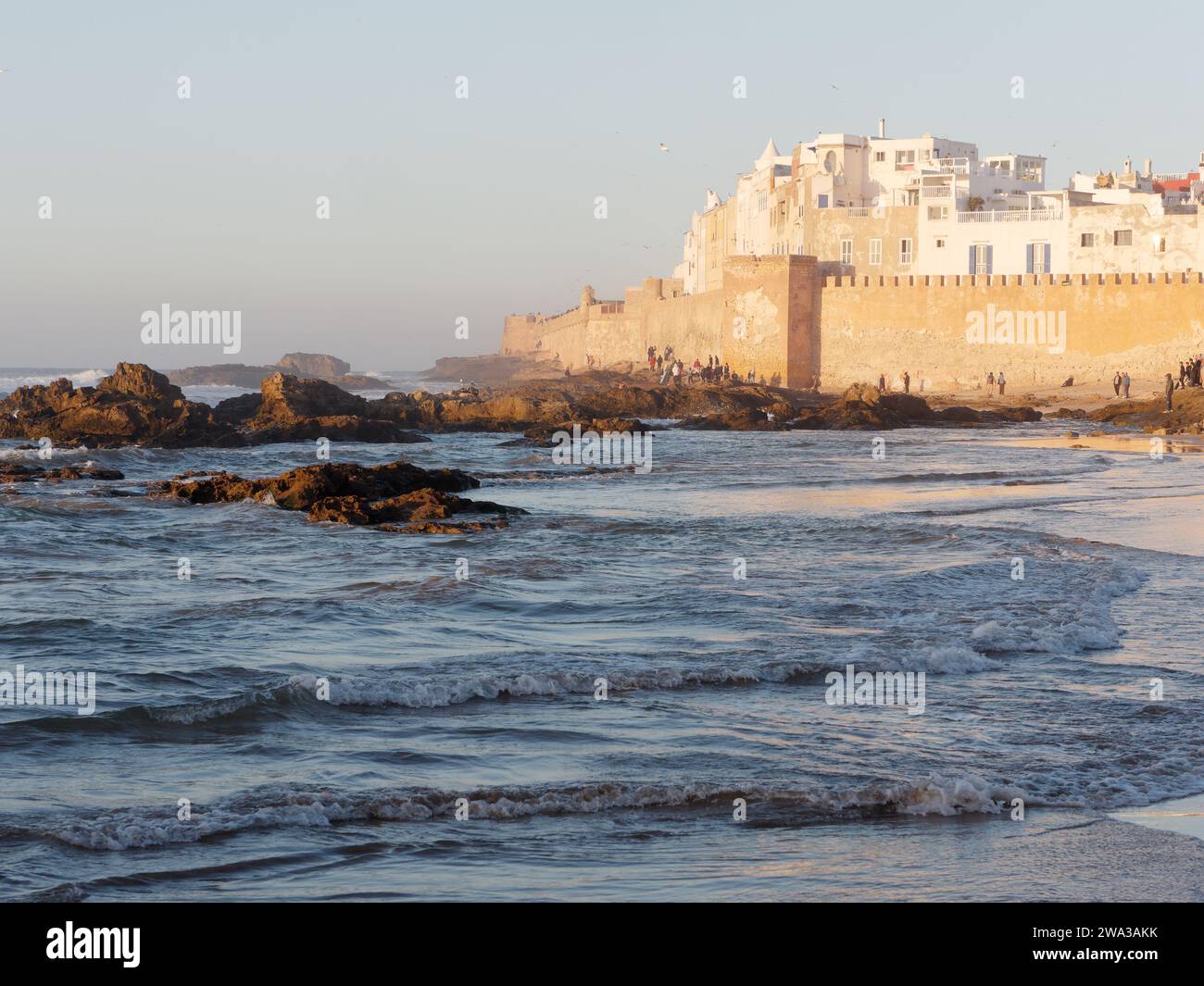 Spiaggia rocciosa con le mura della citta' e la storica medina dietro nella citta' di Essaouira in una serata d'inverno, Marocco, 1 gennaio 2024 Foto Stock