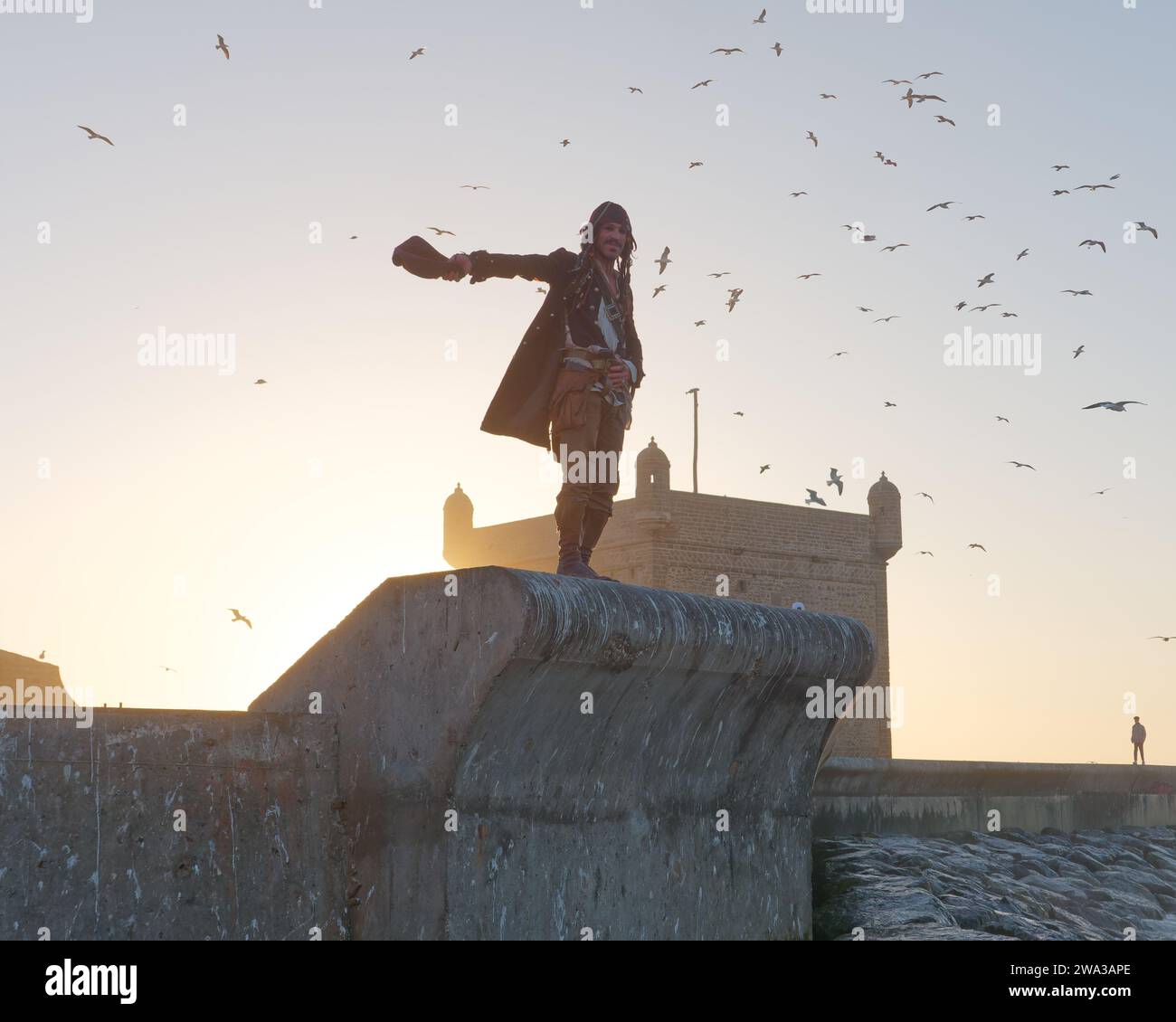 Uomo in costume da pirata cammina per le mura della città vicino al forte in una serata d'inverno nella città di Essaouira, Marocco, 1 gennaio 2024 Foto Stock