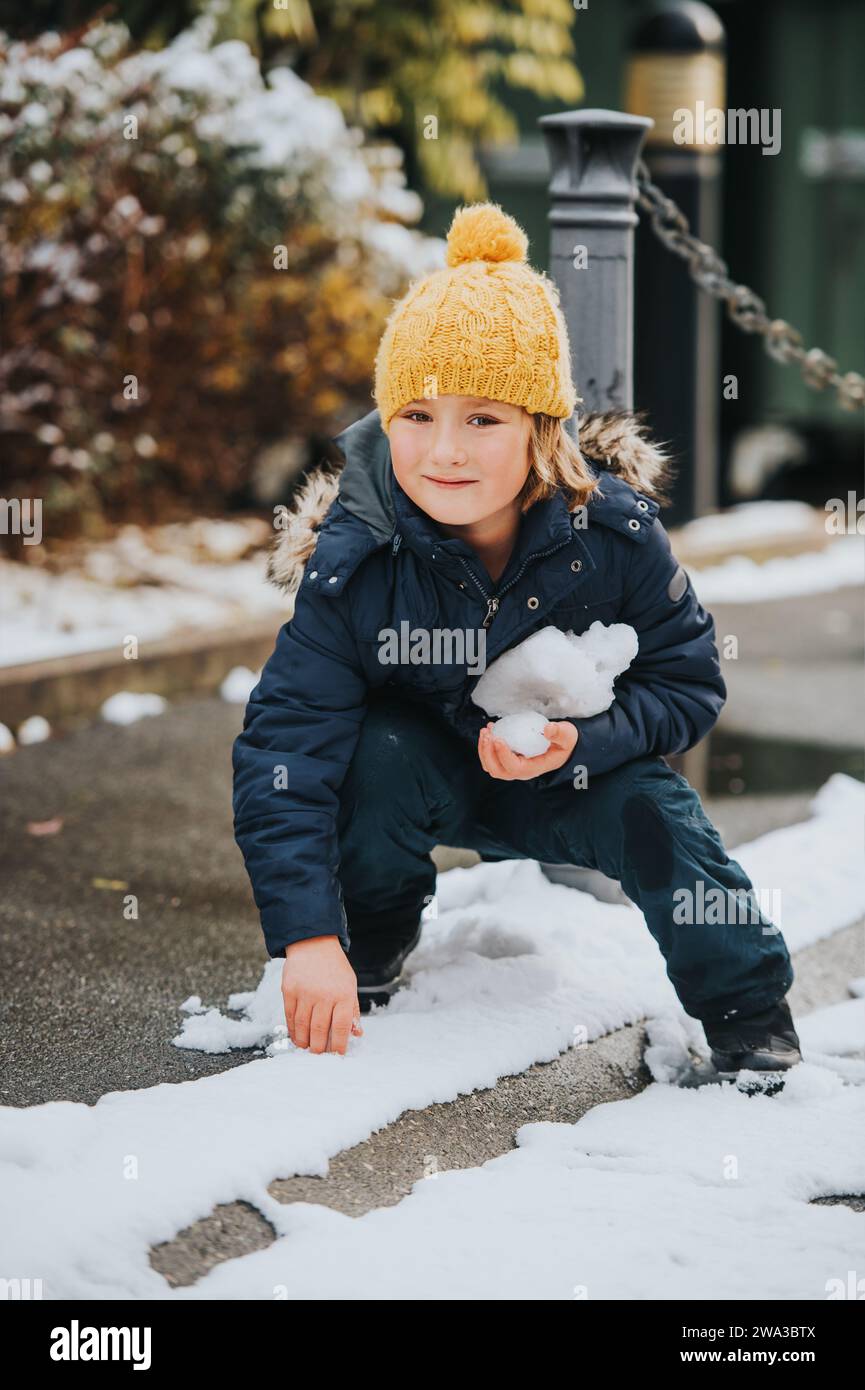 Ritratto all'aperto di un giovane ragazzo di 6 anni che indossa una giacca e degli stivali caldi, che si gode il tempo invernale Foto Stock