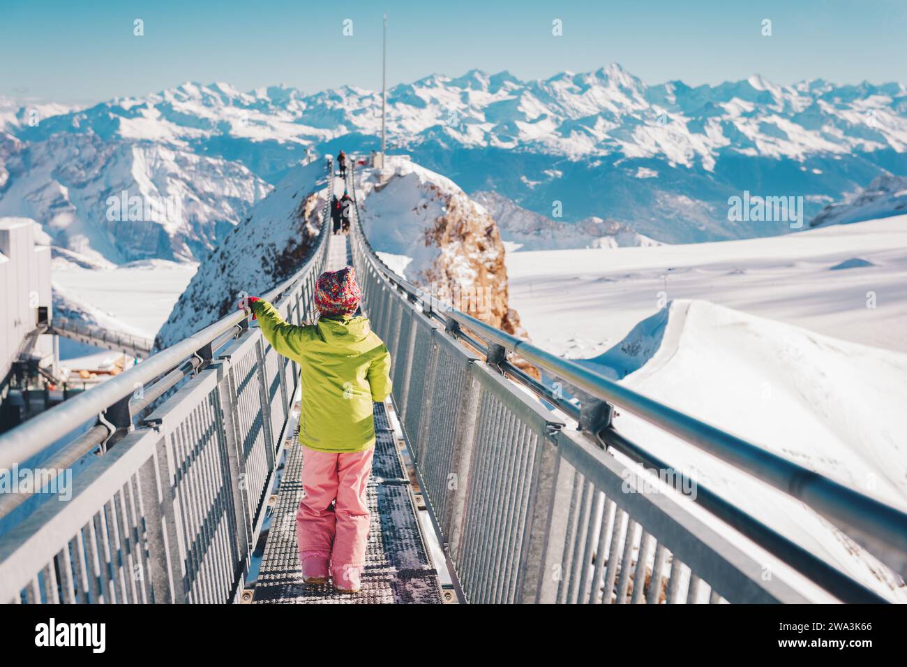 Bambina che gioca con la neve sulla cima della montagna, vacanze invernali con bambini, attività per famiglie sulle Alpi. Vista posteriore. Immagine scattata nel ghiacciaio 300 Foto Stock
